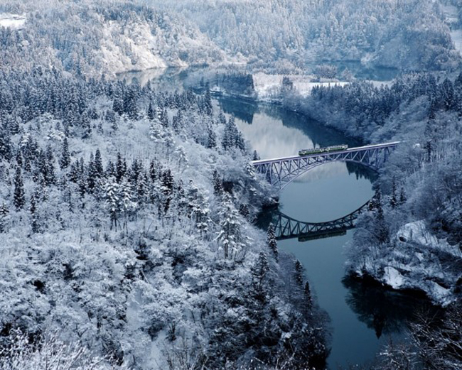 Hình ảnh cây cầu bắc qua dòng sông Tadami phẳng lặng, ven hai bên bờ là rừng cây phủ đầy tuyết trắng, hòa quyện vào nhau tạo nên bức tranh thiên nhiên tuyệt đẹp.
