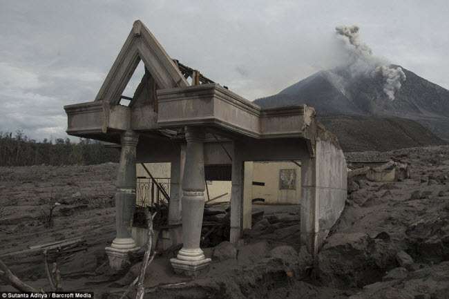 Một lớp tro bụi dày từ nhiều đợt phun trào của núi lửa Sinabung bao phủ quanh một ngôi nhà đổ nát gần chân núi.