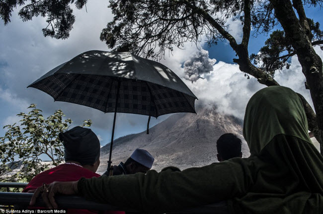 Mọi người ngồi nhìn núi lửa Sinabung hoạt động từ ngôi làng của họ dưới chân núi.