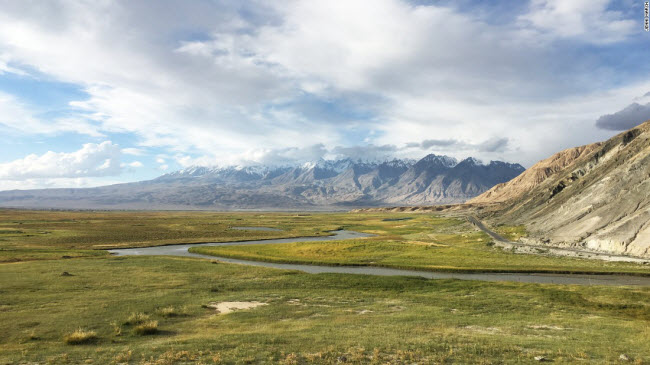 Cánh đồng cỏ xanh mướt xuất hiện dọc tuyến đường Karakoram với dãy núi Thiên Sơn ở phía xa.