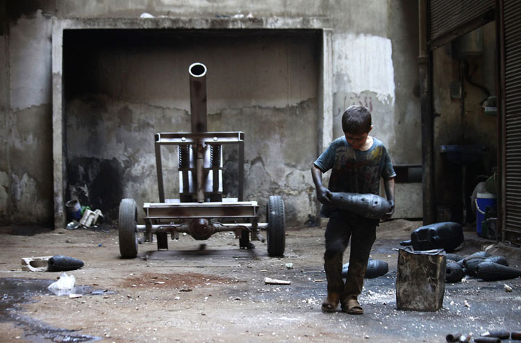 Cậu bé Issa, 10 tuổi đang khệ nệ ôm quả đạn cối vào một xưởng chế tạo vũ khí của quân nổi dậy Syria ở Aleppo hôm 7/9/2013. Issa cùng bố làm việc trong xưởng vũ khí này 10 giờ một ngày, trừ thứ Sáu hàng tuần.

