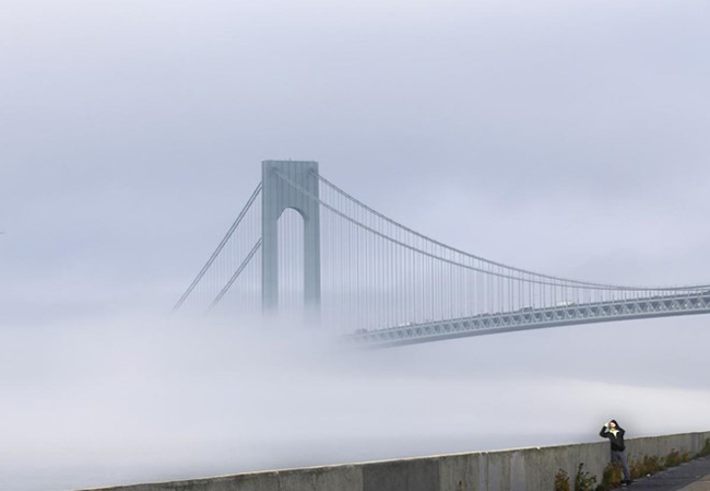 Một người đàn ông dừng lại chụp cảnh sương mù bao phủ cây cầu treo lớn nhất nước Mỹ, Verrazano-Narrows, ngày 12/11. Ảnh: AP.
