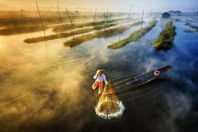 Nhiếp ảnh gia Zay Yar Line đã chia sẻ bức ảnh chụp một ngư dân đang chèo thuyền bằng chân trong khi nơm cá dưới hồ Innlay ở Myanmar.