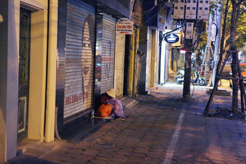 Người vô gia cư mặc áo mưa chống rét, ngủ trên vỉa hè - 1